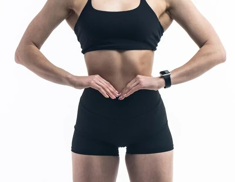 Kobieta w czarnym stroju sportowym pokazująca brzuch i mięśnie