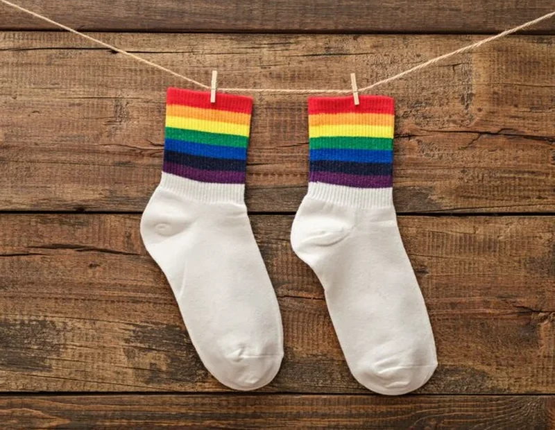 Para białych skarpetek z tęczowym brzegiem na drewnianym tle